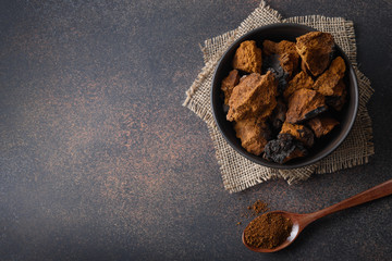 Chaga birch Mushrooms in bowl on black table. Trendy healthy superfood for infusion, tea or coffee....