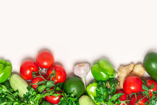 Fresh green and red vegetables on a light background, top view, free space for text. Tomatoes, peppers, avocados, zucchini and parsley flat lay, copy space. Healthy vegetarian food concept.