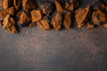 Chaga birch edible mushrooms on natural dark brown table. View from above. Copy space.