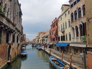 Venetian canal with boats, old low-rise houses, cafe