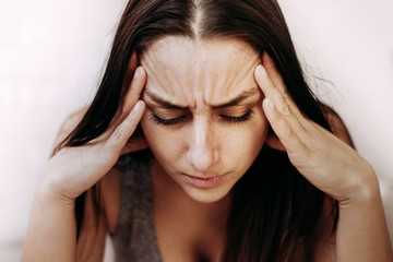 close-up portrait of a young woman with dark hair sitting depressed, holds her head in her hands. I think about problems with work, the financial crisis, illness, epidemic, no money, unemployment