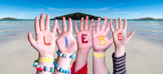 Children Hands Building Colorful German Word Liebe Means Love. Ocean And Beach As Background