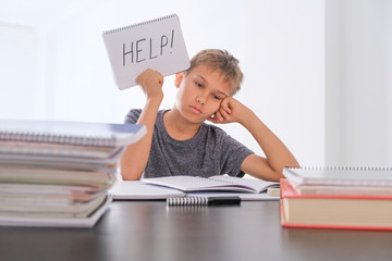 Upset tired preteen child sitting at the table, doing his homework among pile of books. Word Help is written on open notebook