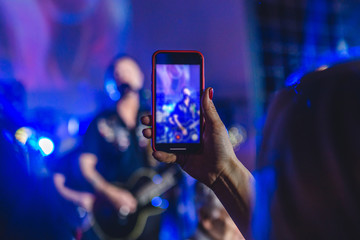 Woman at a concert in the club takes a photo on a smartphone