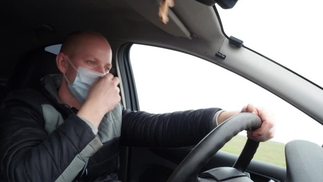 A man driving a car in a protective medical mask. Safe drive in a taxi during a pandemic coronavirus. Protect the driver and passengers from bacteria and virus infection in quarantine