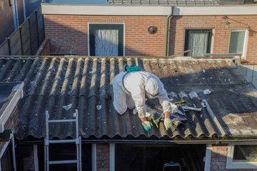 Professional asbestos removal. Man in protective suite removes asbestos roofing.