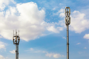 Two telecommunications towers with 4G, 5G transmitters. cellular base station with transmitting antennas on a telecommunications tower against a blue sky with clouds.