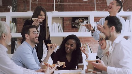 Different ages mixed race business people enjoying lunch together. Older and young multiethnic colleagues eating pizza from box, communicating, having fun, laughing joking together at office.