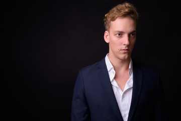 Face of young handsome blond businessman thinking against black background