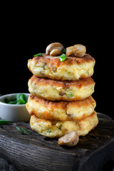 Stack of salty syrniki with champignons and herbs against the black background