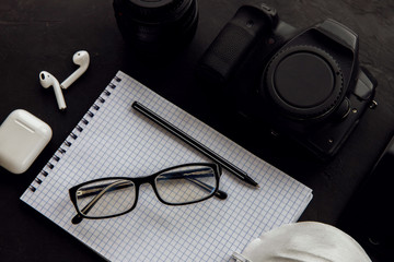 view of the photographer’s desk. On the table lies a camera, lens, telephone, notebook, glasses, pen, telephone, white wireless headphones, a respirator. Business. Flat lay