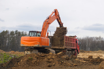 A crawler excavator pours soil into the body of a large truck.