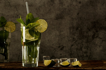 Mojito cocktail with lime, ice cubes and mint in  glass on a black background.Copy space. Mojito cocktail  on a rustic table. Mojito  on a grey stone background.