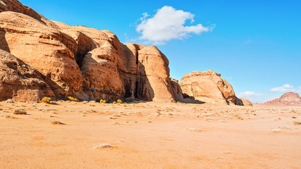 Rocky massifs on red sand desert, bright blue sky in background - typical scenery in Wadi Rum, Jordan