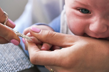 Infant baby boy having his nails cut by mother, detail on scissors and fingertips