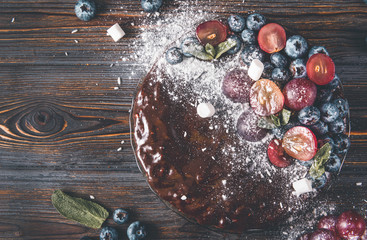 chocolate cake with fresh berries, cake with blueberries, grapes, powdered sugar and mint on a wooden  , top view