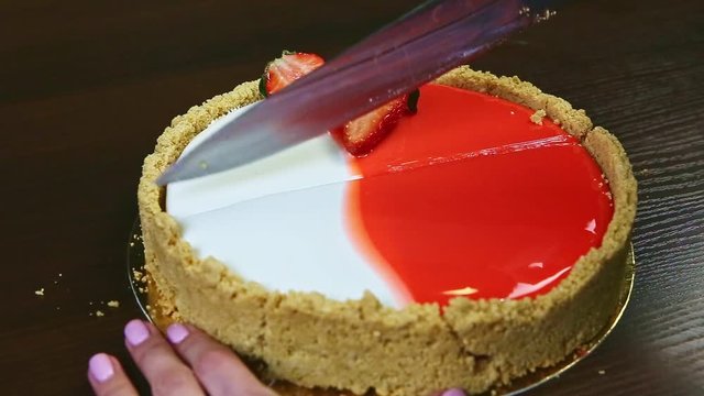 confectioner by hands cuts on half by knife glazed cheesecake with sliced strawberries