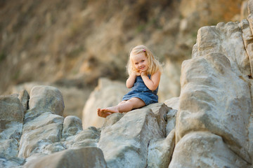little girl sitting on rock at sunset. travel.