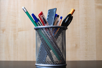 Metal stand with pencils, pens, scissors on wooden table