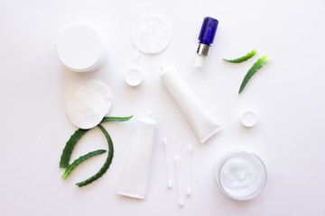 White squeeze tubes, bottles of cream, blue dropper glass serum with aloe vera, cotton pads and buds flat lay on white background top view copy space. Beauty skincare, natural cosmetic. Stock photo.