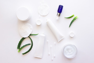 Fototapeta na wymiar White squeeze tubes, bottles of cream, blue dropper glass serum with aloe vera, cotton pads and buds flat lay on white background top view copy space. Beauty skincare, natural cosmetic. Stock photo.