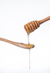 sweet Golden honey flows down a wooden stick on a wooden spoon on a white background.