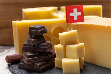 Tasty Swiss food, block of medium-hard yellow cheese emmental or emmentaler with round holes, matured gruyere and high quality milk chocolate served in cubes as mountains top with Swiss flag.