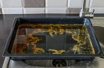 Dirty, greasy baking sheet for the oven is on the washbasin