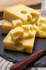 Block of Swiss medium-hard yellow cheese emmental or emmentaler with round holes and cheese knife - obrazy, fototapety, plakaty