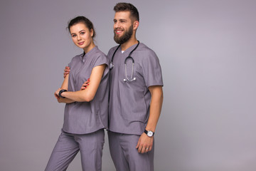 doctors relationship. male and female nurses in gray medical costumes with stethoscope on neck are standing fashion with smiles on the gray wall background, medical concept, free space on right side