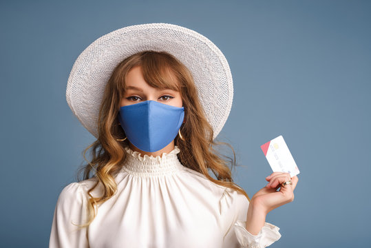 Spring, summer online shopping during quarantine conception: fashionable woman wearing protective mask posing with plastic bank card. Blue background