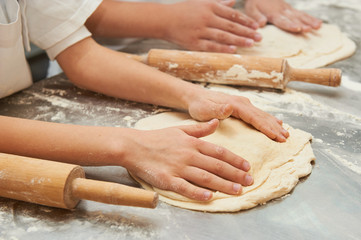 Little kids make dough products. Flour is scattered around. Hands close up.