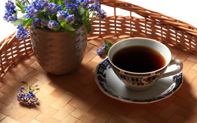Ð¡up of coffee and a bouquet of blue field forget-me-not flowers on a wicker table