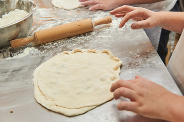 Little kids make dough products. Flour is scattered around. Hands close up.