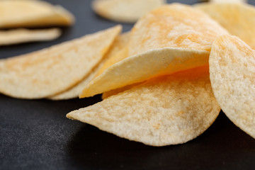 Classic potato chips. Fast food snack isolated on black background. A pile of crispy chips close-up as a background. Unhealthy food.