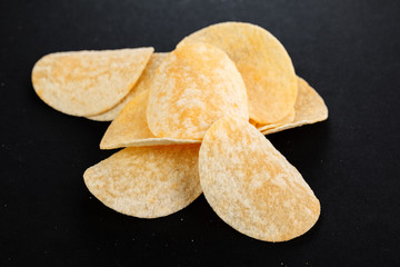 Classic potato chips. Fast food snack isolated on black background. A pile of crispy chips close-up as a background. Unhealthy food.
