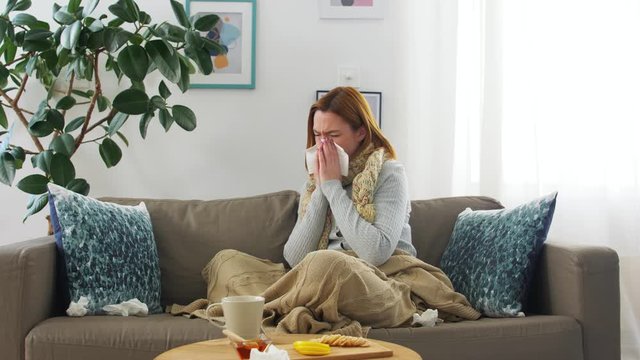 healthcare, cold, allergy and people concept - sick woman blowing her runny nose in paper tissue at home