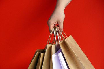 Hand with white paper bags and craft on bright red background. Season of sales or purchases as gift for holidays. Christmas shopping. Courier delivery of products in eco-friendly packaging. copy space