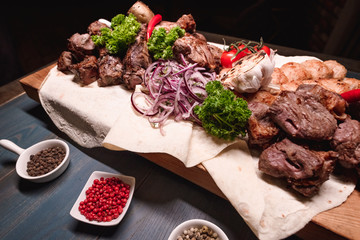 Appetizing fried meat lies on a wooden tray, among the seasonings. Studio photography of food in the cooking industry, dark background