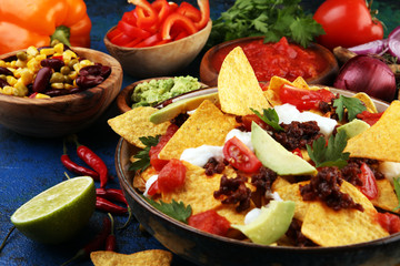 mexican nacho chips garnished with ground beef, guacamole, melted cheese, peppers and cilantro leaves in plate