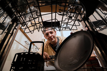 A young man puts a frying pan in the dishwasher. Inside view of a dishwasher. Washing dirty dishes...