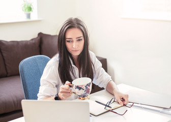 Portrait of attractive dark haired woman drinking coffee while working from home  , freelance business woman
