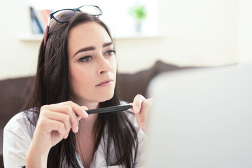 Portrait of attractive dark haired woman  working from home, reading emails on laptop ,  freelance young beautiful businesswoman making money from home