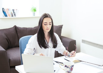 Portrait of attractive dark haired woman  working from home, reading emails on laptop ,  freelance young beautiful businesswoman making money from home
