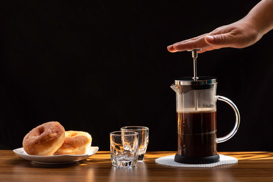 Coffee brewing in a French press pot and two donuts in plate on the wood table and warm morning light, Selective focus.