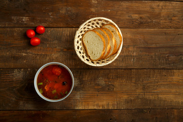 A plate of Italian tomato soup with potatoes and mushrooms on a wooden table and bread.