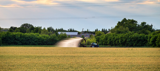 Obraz premium Tractor watering and sprays field and tillage. Scenic agricultural land and farm. Agriculture. Cultivations the soil sowing, panoramic banner. Harvester in meadow irrigation. 