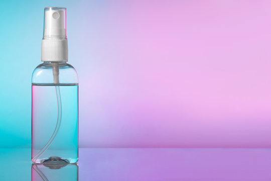 Bottle instant antiseptic hand sanitizer atomizer pump, mist spray in transparent plastic container. Antibacterial alcohol liquid, disinfectant with extracts, Pink, magenta, blue gradient background.