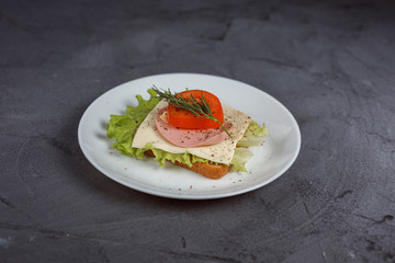 sandwich with ham, cheese, lettuce and tomato with greens on white plate.