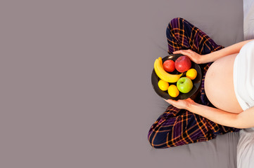 Healthy Nutrition During Pregnancy. Concept of expectation of the child, pregnancy and motherhood. Young pregnant woman sits at home in bed with plate of fresh fruit. Happy pregnancy, waiting for baby